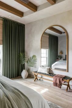 a bedroom with a bed, mirror and bench in front of a window that has green drapes