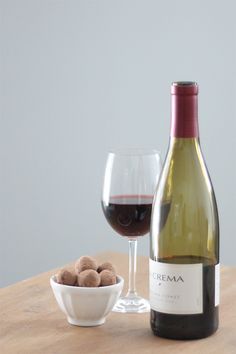 a bottle of wine next to a bowl of chocolates and a glass of wine