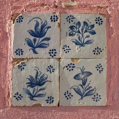 four blue and white tiles on the side of a pink wall with flowers in them