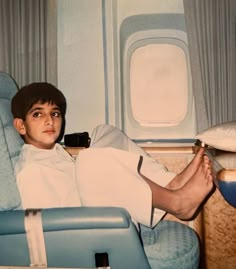 a boy sitting in an airplane with his feet propped up on the seat and looking at the camera