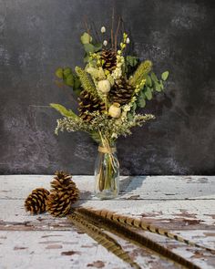 a vase filled with lots of flowers next to a pine cone