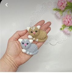 two small crocheted cats sitting on top of each other in someone's hand