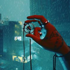 a hand holding an object in the middle of a city at night with rain falling on it