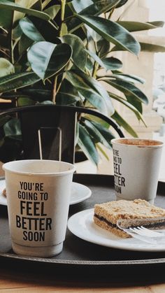 two coffee cups and one sandwich on a tray with plants in the backround