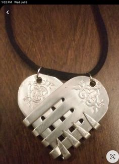 a silver heart shaped pendant on a black cord necklace with an intricate design in the shape of a hand