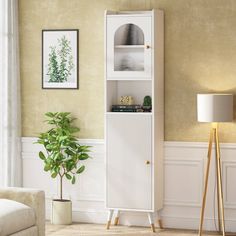 a living room with a white cabinet next to a lamp and a potted plant