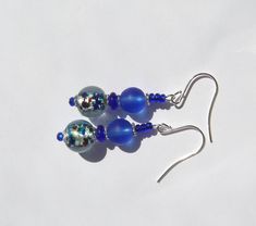 These earrings are made with gorgeous vintage foil glass beads with blues, greens, aquas, and amber speckles that have been combined with deep blue matte glass beads and accented with glittery royal blue seed beads. Hanging Length: 2 inches. Ear wires: silver plated surgical steel. Blue Round Beaded Earrings With Spacer Beads, Blue Earrings With Spacer Beads For Gift, Blue Round Bead Glass Earrings, Blue Glass Round Bead Earrings, Blue Glass Round Beads Earrings, Blue Czech Glass Beaded Earrings, Blue Glass Earrings With Round Beads, Blue Czech Glass Beaded Earrings With Dangling Beads, Blue Glass Beaded Earrings With Ear Wire