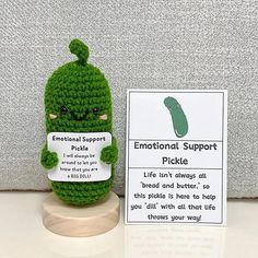 a small green stuffed animal sitting on top of a wooden stand next to a sign