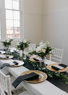 the table is set with black and gold plates, napkins, and greenery