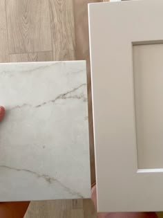 a person is holding up a white frame with a marble pattern on the front and side