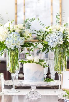 three vases filled with white and blue flowers on top of a table