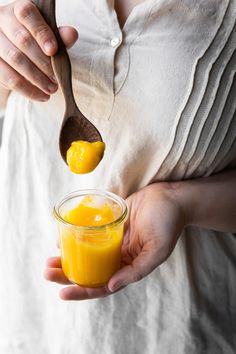 a woman is holding a spoon with some orange juice in it and she is about to scoop into the jar