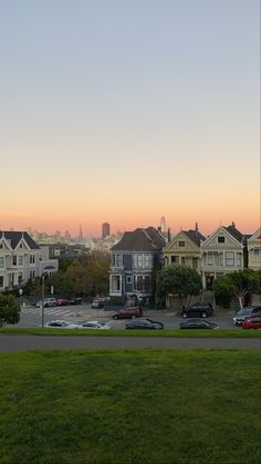 a view of some houses from across the street at sunset, with cars parked on the road