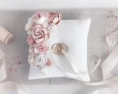 the ring pillow is decorated with flowers and ribbons on it's side, along with two wedding rings