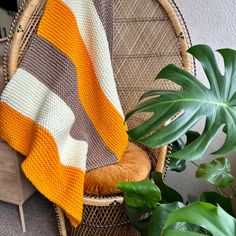 a wicker chair with a blanket on it next to a potted green plant