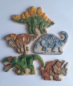 four dinosaur cookies are shown on a white surface