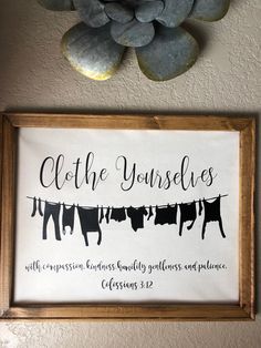 a framed sign with clothes hanging from it's clothesline next to a potted plant