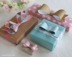 three small gift boxes with bows and paper decorations on the top one is blue, pink, and white