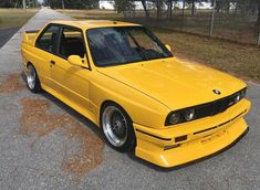 a yellow car parked on the side of a road next to a fence and trees