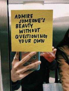 a woman holding up a yellow sign that says admire someone's beauty without questioning your own