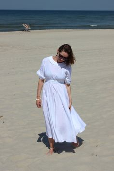 a woman standing on top of a sandy beach next to the ocean wearing a white dress