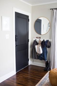 a black door and coat rack in a room with white walls, hardwood floors and a mirror on the wall