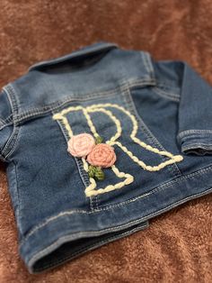 a denim jacket with embroidered letters and flowers on the back, sitting on a bed