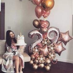 a woman sitting on a couch next to a cake and balloons in the shape of numbers