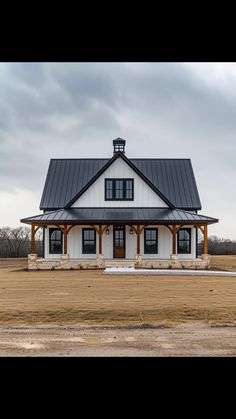 a white house with a black roof in the middle of an open field on a cloudy day