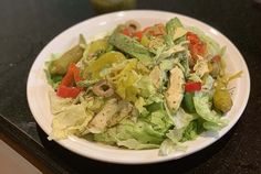 a white plate topped with a salad on top of a black counter next to a bottle