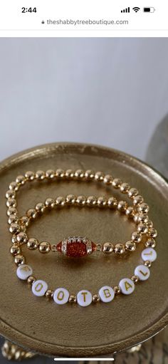 two gold bracelets with white and red beaded beads on a metal tray in front of a vase