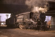 an old steam train traveling under a bridge