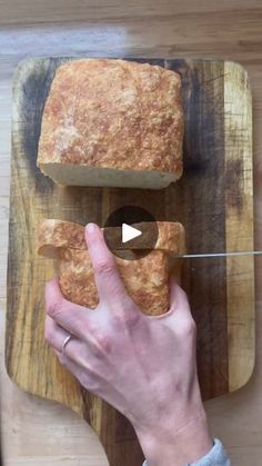 a person cutting bread on top of a wooden cutting board