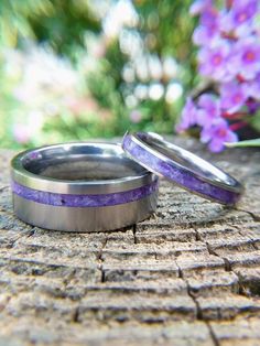 two wedding rings with purple and silver inlays sitting on a piece of wood