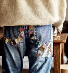 a person standing in front of a wooden table wearing jeans with colorful patches on them