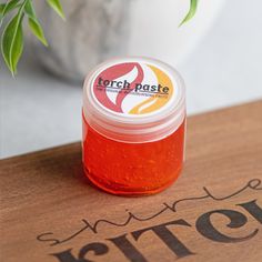 a small jar of orange colored paste sitting on top of a wooden table next to a potted plant