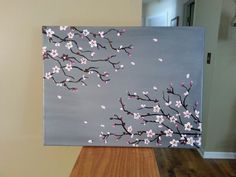 a painting with pink flowers on it sitting on top of a wooden floor next to a wall