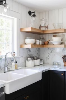 a kitchen with black cabinets and white marble counter tops, open shelving above the sink