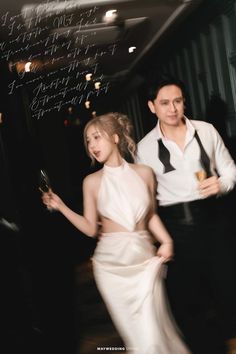 a man and woman in formal wear walking down a hall way with writing on the wall behind them