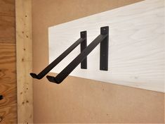 a pair of black brackets mounted to the side of a wood paneled wall next to a piece of plywood