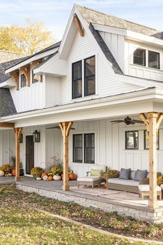 a white house with lots of windows and porch furniture on the front lawn, surrounded by fall foliage