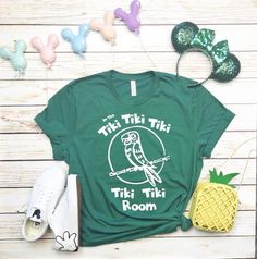 a t - shirt that says this tiki room next to some pineapples