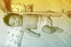 a baby laying on top of a bed next to a measuring tape