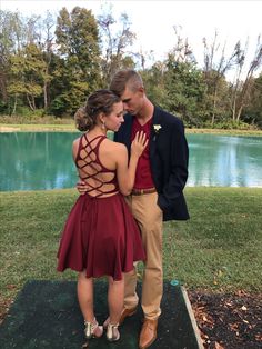 a man and woman standing next to each other in front of a lake