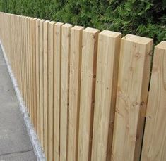 a wooden fence next to a sidewalk and some bushes on the side of the road