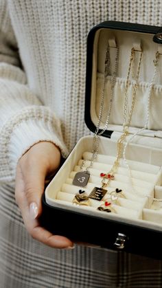 a person holding an open jewelry box with necklaces and rings in it's lid