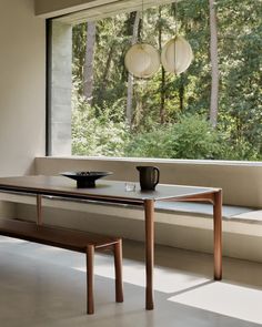 a wooden table sitting in front of a window next to a cup and bowl on top of it