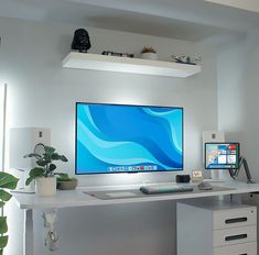 a computer desk with two monitors and a keyboard on it, in front of a white wall