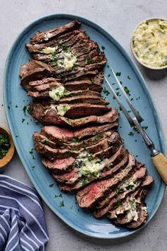 a blue plate topped with sliced up steak next to a bowl of mashed potatoes