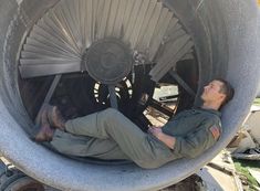 a man laying on the ground in front of a large metal object that looks like a propeller